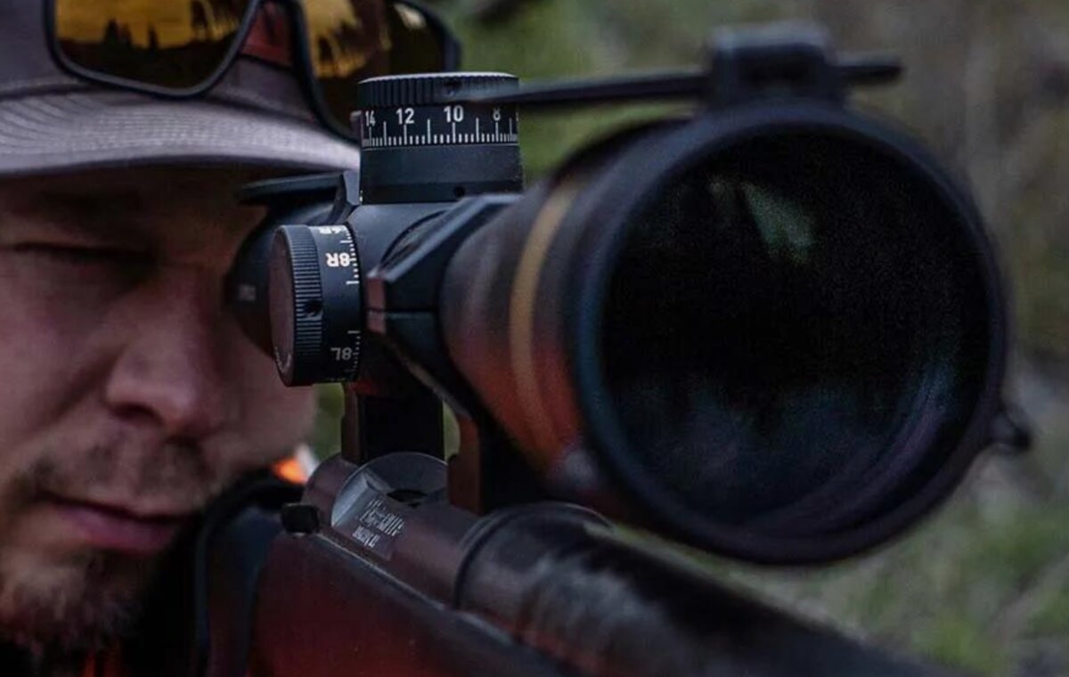A shooter sighting through a rifle scope on a range